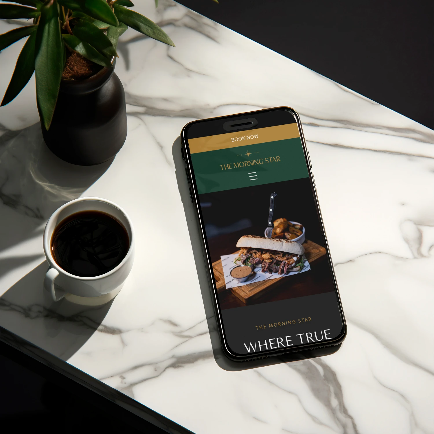 Phone on a marble surface displaying a gastro pub website design alongside a coffee cup, designed by Dream Wild Studio