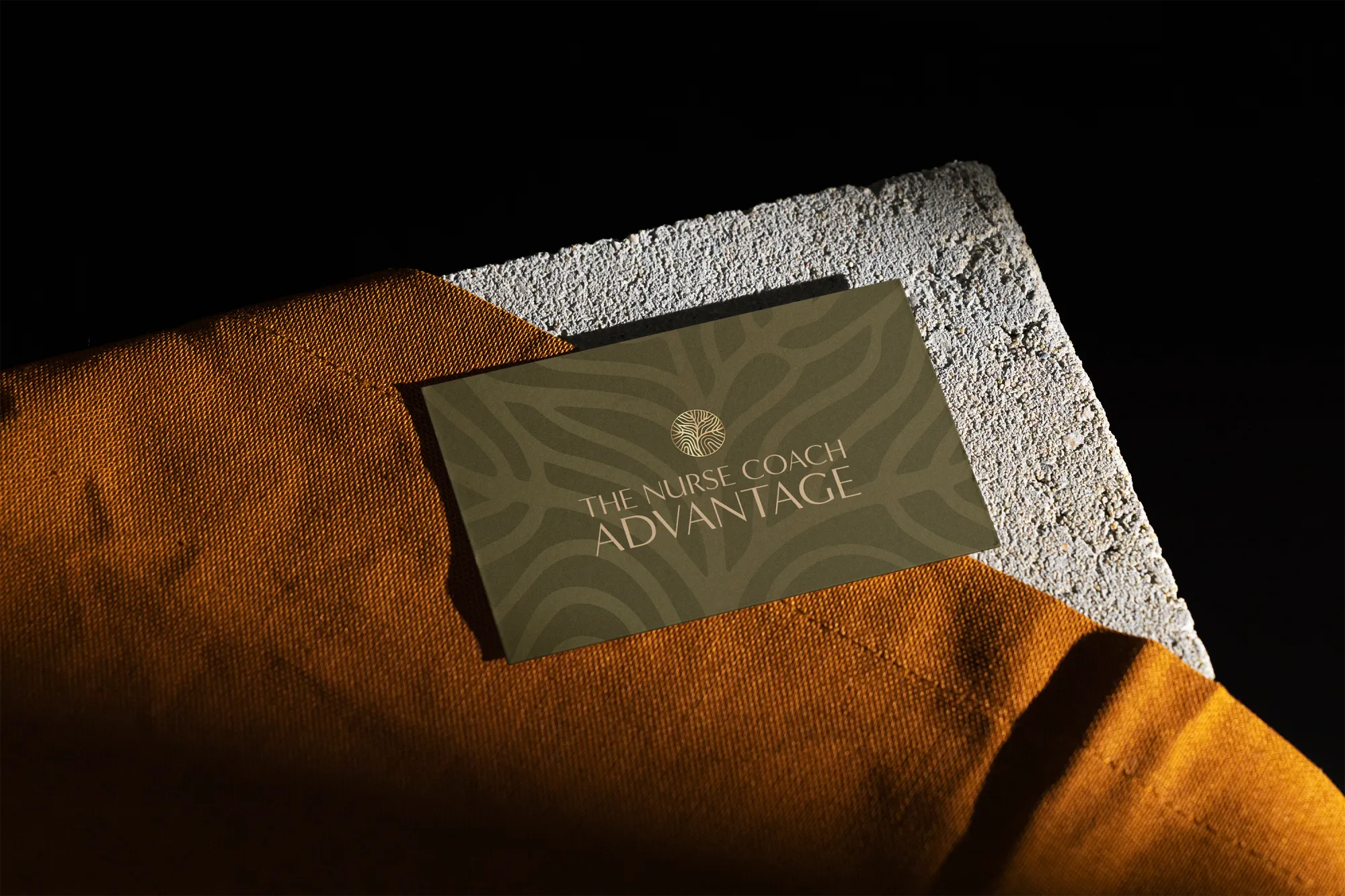 Logo design on a business card for nurse coach and their wellness business, featuring a deep olive background with subtle organic patterns and gold lettering, placed on a textured surface. Branding by Dream Wild Studio.