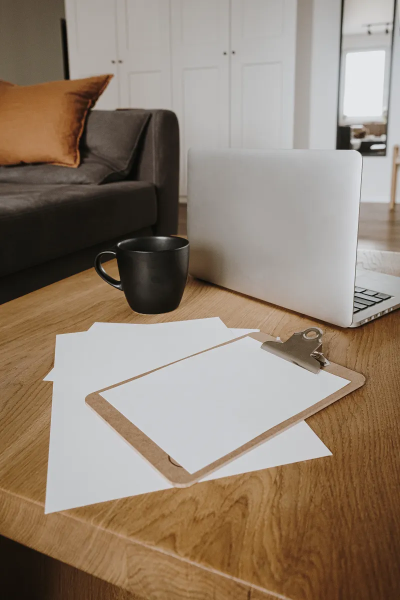 Laptop, black mug and clipboard with blank notepaper on a wooden desk, ready for a Dream Wild Power Hour session.

