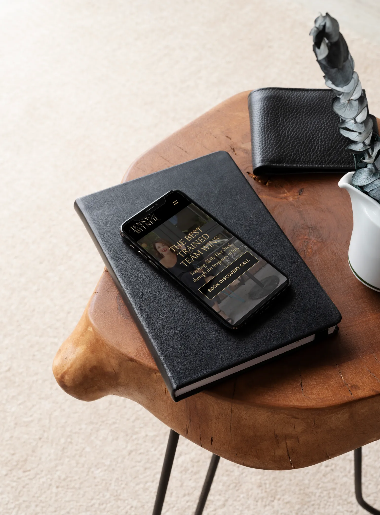 Jenny Bitner website displayed on a phone resting on a book in a styled setting for a female entrepreneur and coach, website design by Dream Wild Studio