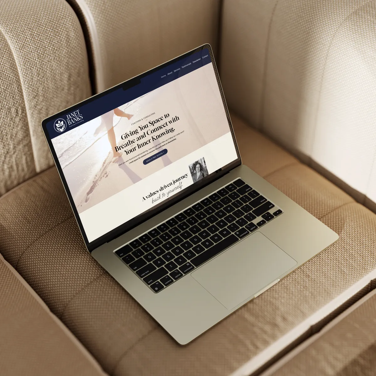 Janet Banks coaching website on a laptop sitting on a cream upholstered chair, web design by Dream Wild Studio.